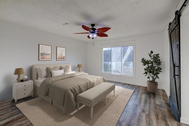 bedroom with a barn door, ceiling fan, dark wood-type flooring, and a textured ceiling