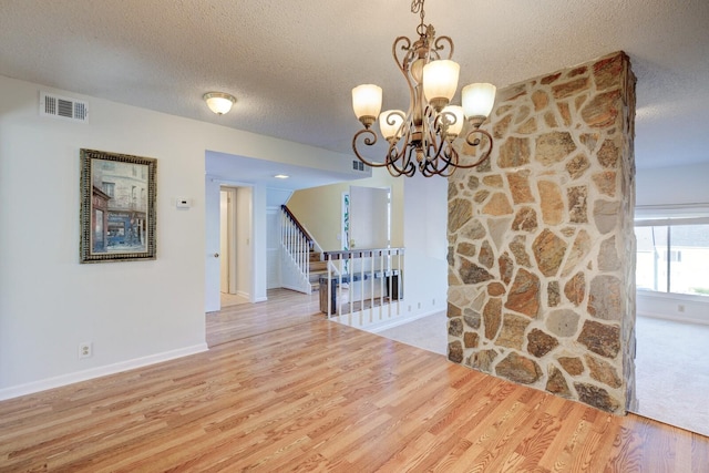 unfurnished dining area with light wood-type flooring, a textured ceiling, and an inviting chandelier