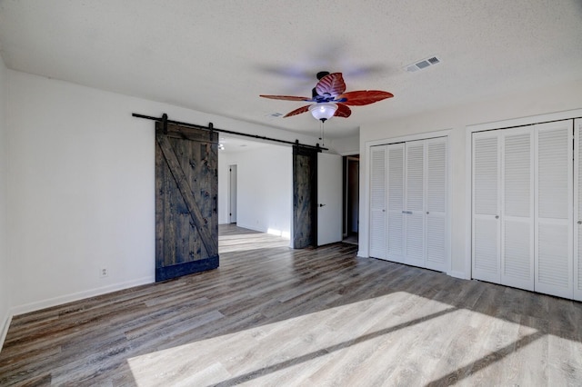 unfurnished bedroom featuring a textured ceiling, two closets, ceiling fan, a barn door, and hardwood / wood-style flooring