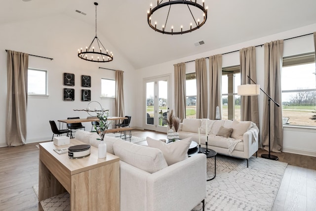 living room featuring lofted ceiling, light wood-type flooring, french doors, and an inviting chandelier