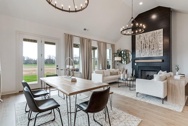 dining space with a large fireplace, light hardwood / wood-style flooring, an inviting chandelier, and vaulted ceiling