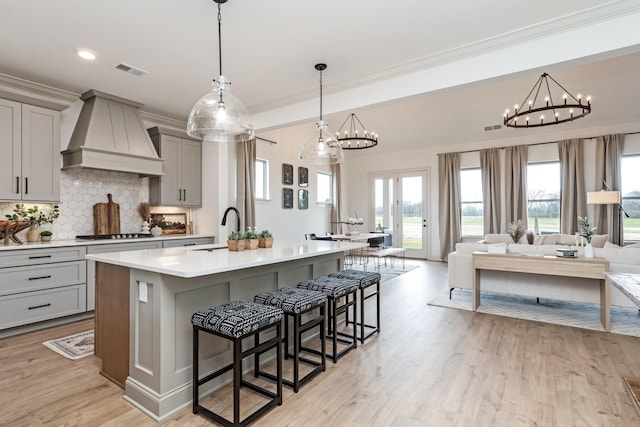 kitchen featuring gray cabinetry, a kitchen island with sink, sink, decorative backsplash, and custom range hood