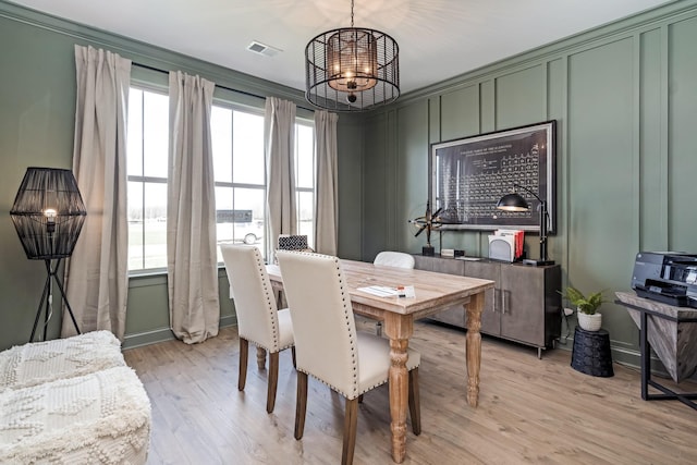 dining space with light hardwood / wood-style floors, crown molding, and an inviting chandelier