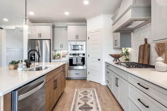 kitchen featuring premium range hood, hanging light fixtures, sink, appliances with stainless steel finishes, and white cabinetry