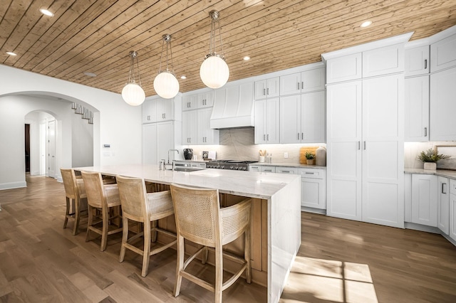 kitchen featuring pendant lighting, premium range hood, white cabinetry, and a kitchen island with sink