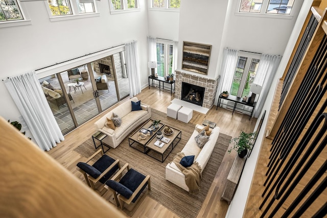 living room with light wood-type flooring, a towering ceiling, and a brick fireplace