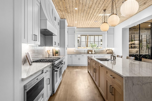 kitchen featuring sink, pendant lighting, a center island with sink, range with two ovens, and white cabinets