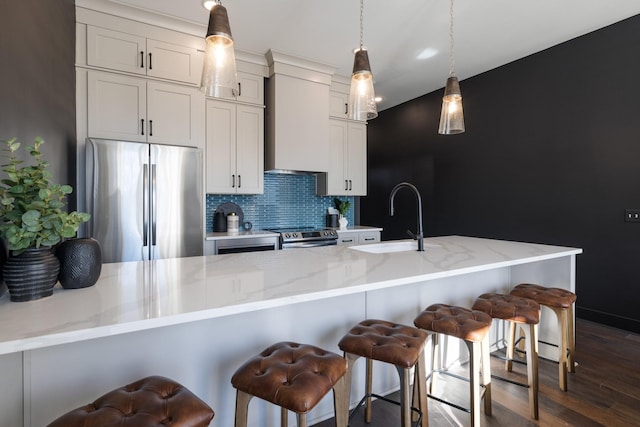 kitchen featuring stainless steel appliances, tasteful backsplash, wall chimney range hood, a breakfast bar, and sink