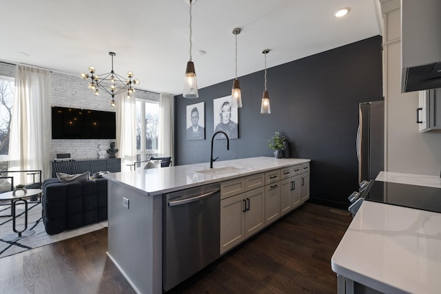 kitchen featuring dark wood-type flooring, stainless steel appliances, sink, hanging light fixtures, and a kitchen island with sink