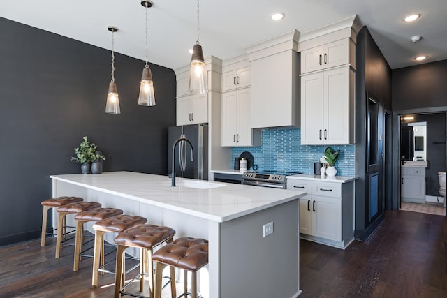 kitchen featuring appliances with stainless steel finishes, decorative light fixtures, decorative backsplash, light stone counters, and a center island with sink