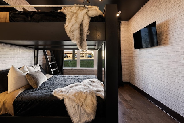 bedroom featuring dark wood-type flooring and brick wall