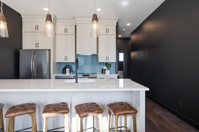 kitchen featuring backsplash, white cabinetry, light stone countertops, a breakfast bar area, and stainless steel fridge