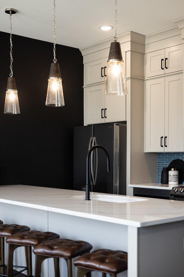 kitchen featuring tasteful backsplash, refrigerator, hanging light fixtures, a kitchen breakfast bar, and light stone counters