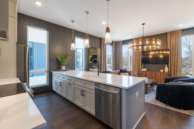 kitchen with appliances with stainless steel finishes, sink, hanging light fixtures, dark hardwood / wood-style floors, and a center island with sink