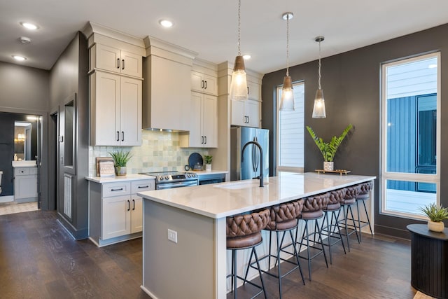 kitchen with dark hardwood / wood-style floors, wall chimney range hood, pendant lighting, a breakfast bar area, and stainless steel appliances