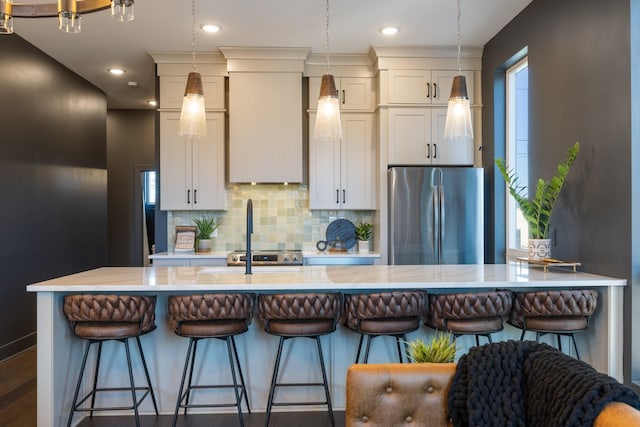 kitchen featuring backsplash, a kitchen bar, white cabinetry, stainless steel fridge, and light stone counters