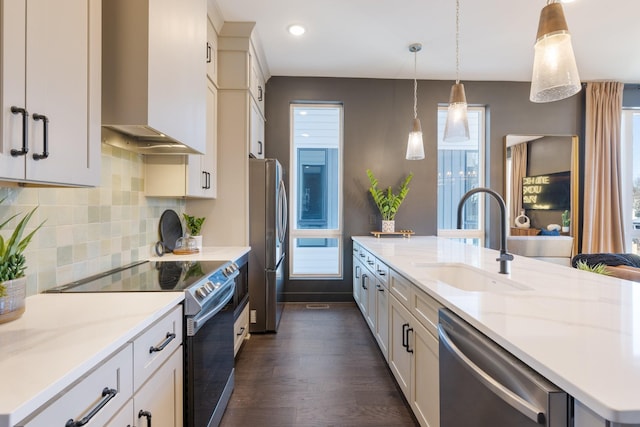 kitchen with stainless steel appliances, hanging light fixtures, wall chimney exhaust hood, light stone counters, and sink