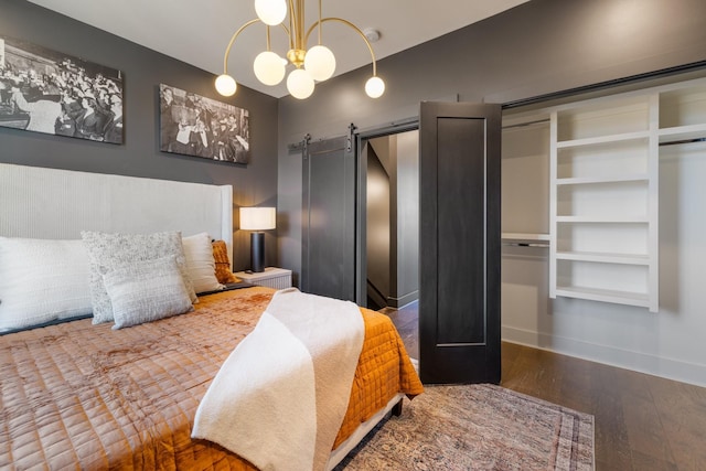 bedroom featuring dark wood-type flooring, a barn door, and an inviting chandelier