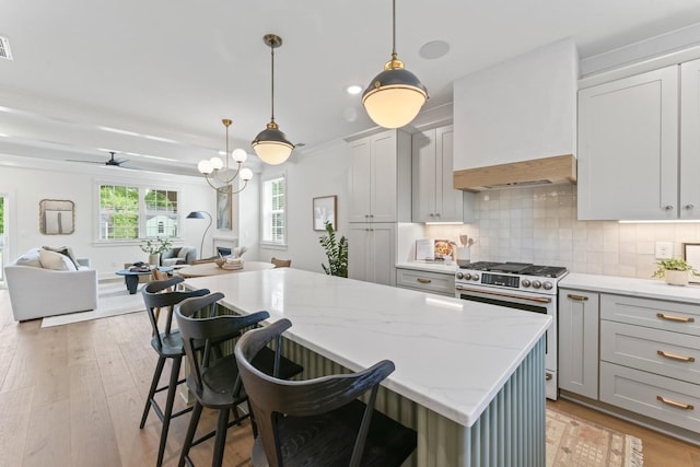 kitchen featuring stainless steel range, tasteful backsplash, premium range hood, decorative light fixtures, and a breakfast bar area