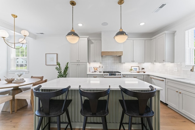 kitchen with light stone countertops, hanging light fixtures, a kitchen breakfast bar, high end stove, and decorative backsplash