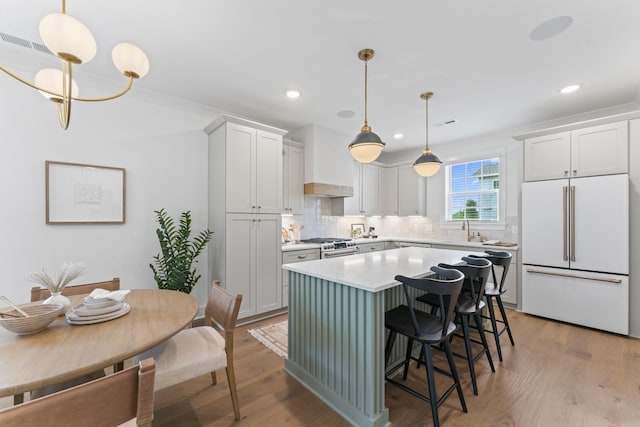 kitchen with built in fridge, custom exhaust hood, white cabinetry, and hanging light fixtures