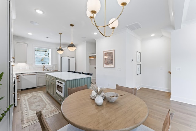 dining room with a notable chandelier, light hardwood / wood-style floors, ornamental molding, and sink