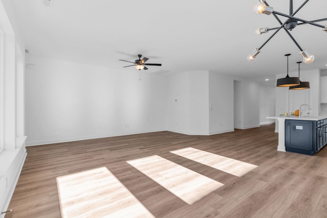 unfurnished living room with ceiling fan with notable chandelier, light hardwood / wood-style floors, and sink