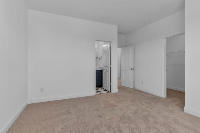 unfurnished bedroom with light carpet, ensuite bath, a spacious closet, and a closet