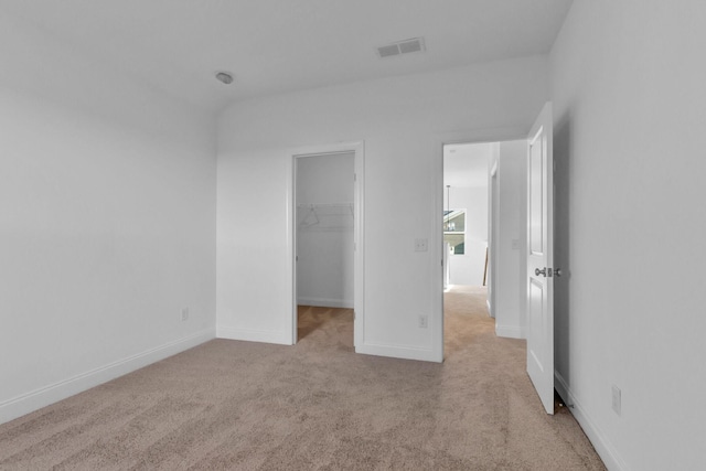 unfurnished bedroom with a walk in closet, light colored carpet, and a closet