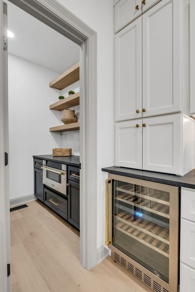 bar featuring light hardwood / wood-style floors, white cabinetry, beverage cooler, and stainless steel oven