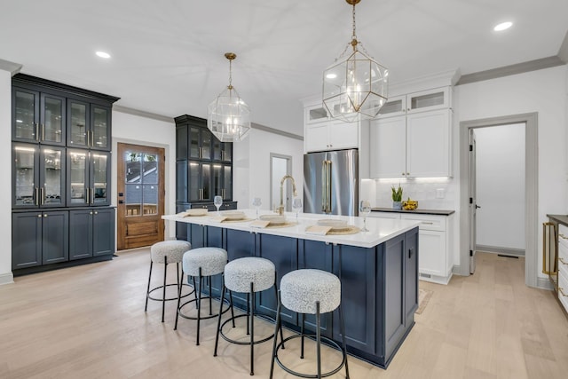 kitchen featuring hanging light fixtures, high quality fridge, ornamental molding, and an island with sink