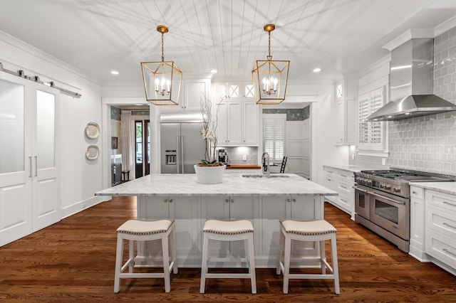 kitchen featuring high quality appliances, a center island with sink, a kitchen breakfast bar, wall chimney range hood, and decorative backsplash