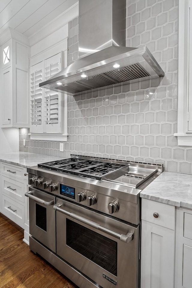 kitchen featuring double oven range, backsplash, white cabinets, wall chimney range hood, and light stone countertops