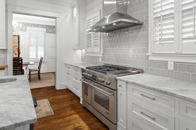 kitchen with dark wood-type flooring, white cabinets, range with two ovens, wall chimney exhaust hood, and tasteful backsplash