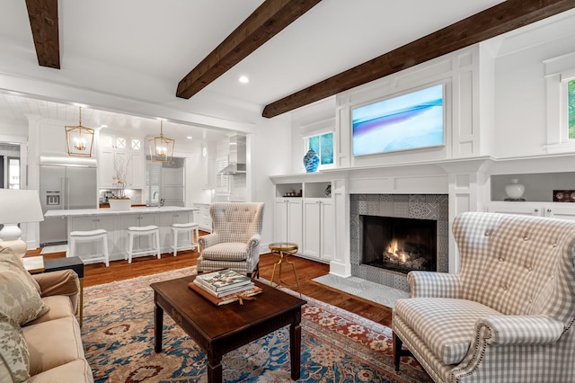 living room with a tile fireplace, beamed ceiling, dark wood-type flooring, and sink