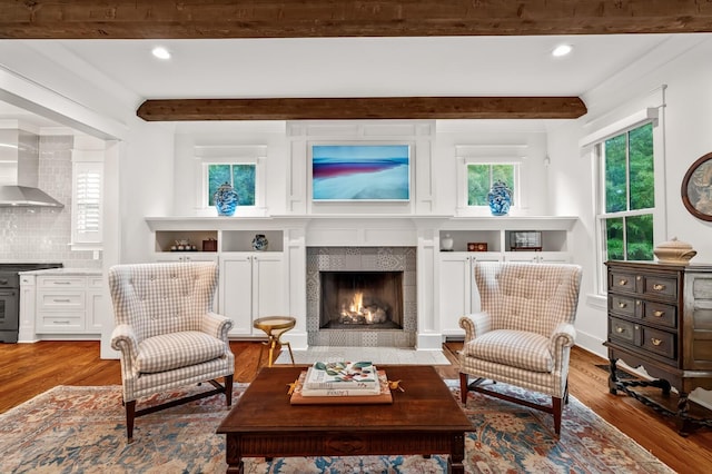 living area featuring beamed ceiling, hardwood / wood-style floors, and a tiled fireplace