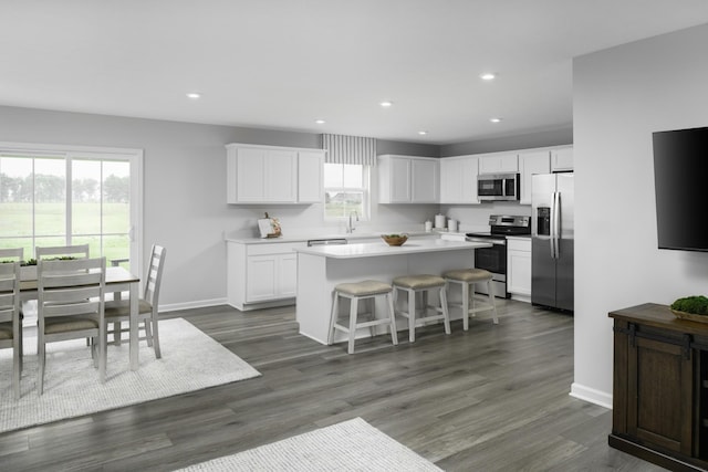 kitchen featuring a kitchen bar, appliances with stainless steel finishes, dark wood-type flooring, white cabinets, and a center island