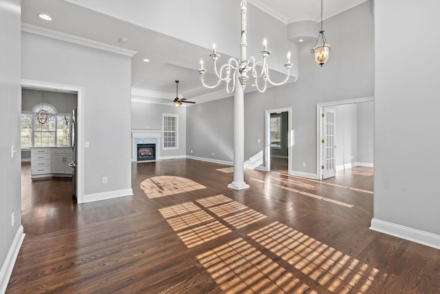 unfurnished living room with dark hardwood / wood-style flooring, ceiling fan with notable chandelier, crown molding, a fireplace, and a high ceiling