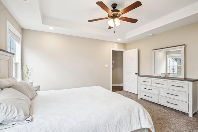 carpeted bedroom featuring multiple windows, a tray ceiling, and ceiling fan