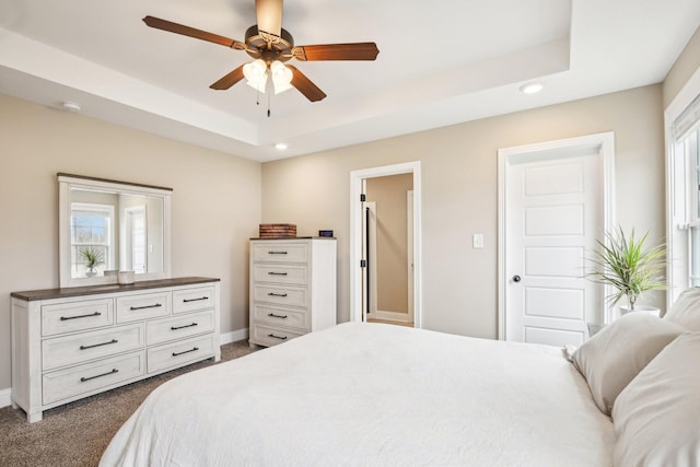 bedroom featuring dark colored carpet, ceiling fan, and a tray ceiling