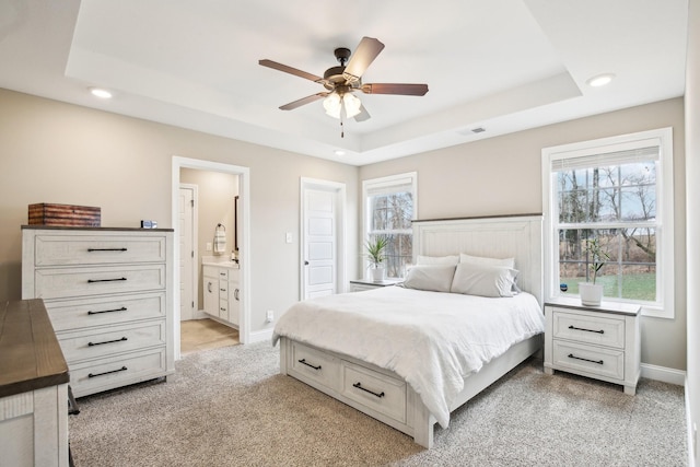 carpeted bedroom with a raised ceiling, ensuite bath, and ceiling fan