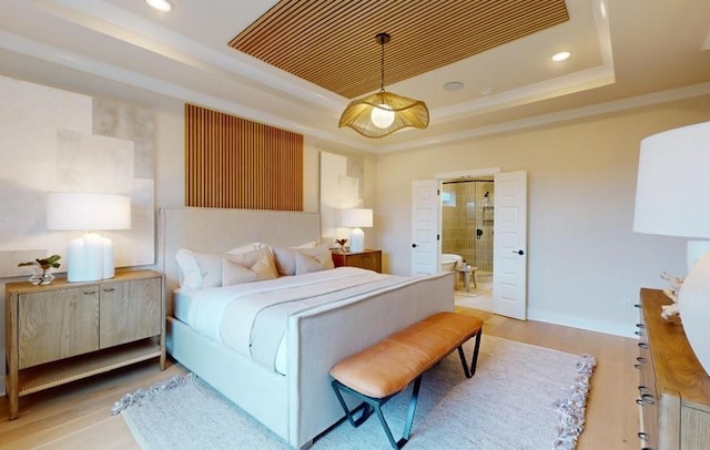 bedroom featuring ensuite bath, light hardwood / wood-style flooring, and a raised ceiling