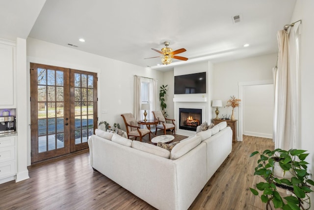 living area with a glass covered fireplace, french doors, visible vents, and wood finished floors