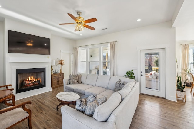 living area with recessed lighting, visible vents, a lit fireplace, and wood finished floors