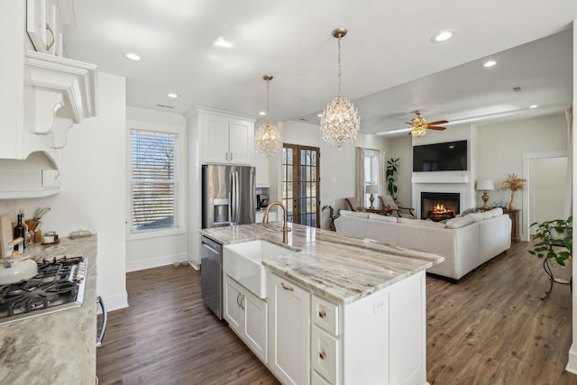 kitchen with a lit fireplace, appliances with stainless steel finishes, dark wood-style floors, white cabinets, and a sink