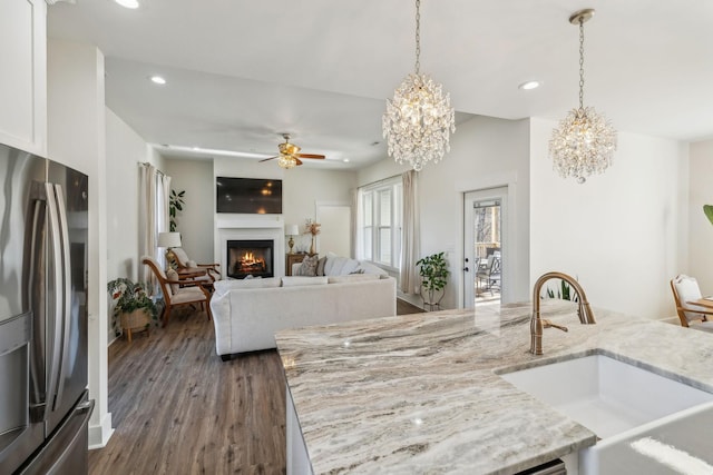 kitchen with light stone counters, stainless steel fridge with ice dispenser, recessed lighting, a warm lit fireplace, and a sink