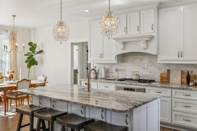 kitchen featuring stainless steel gas cooktop, a chandelier, custom range hood, decorative backsplash, and white cabinetry