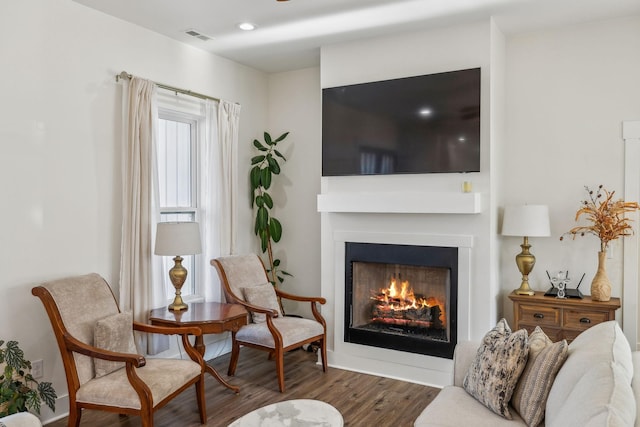 living area featuring recessed lighting, wood finished floors, visible vents, and a warm lit fireplace