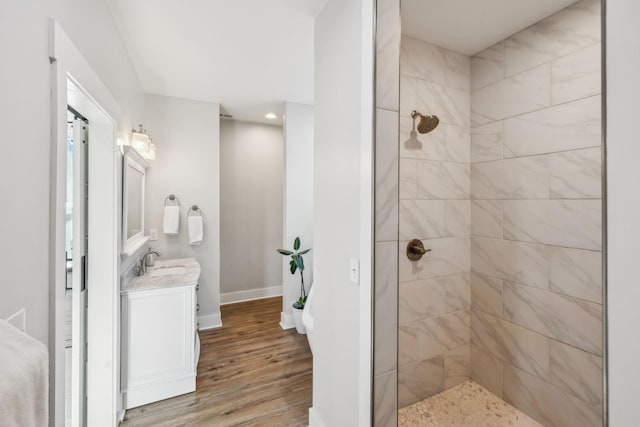 full bath featuring vanity, wood finished floors, baseboards, and a tile shower