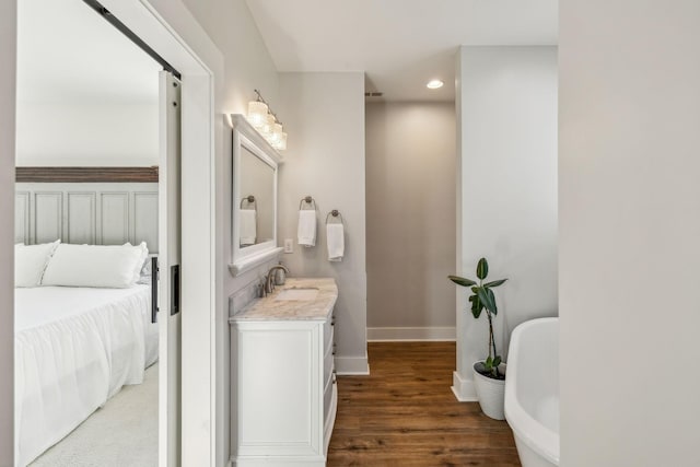 bathroom featuring vanity, wood finished floors, baseboards, a freestanding tub, and recessed lighting